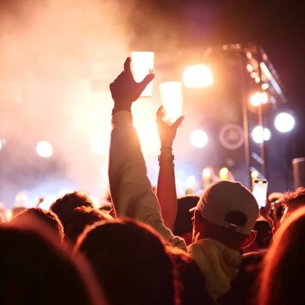 Menschenmenge bei Konzert mit erhobenen Händen, die Plastikbecher halten